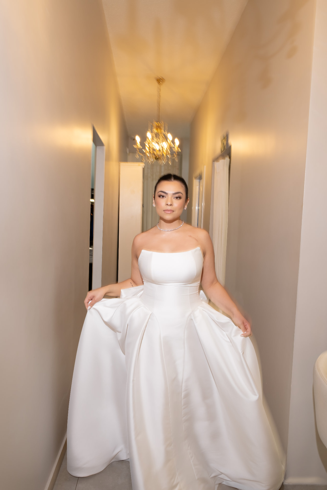 Noiva segurando a saia do vestido sob um lustre